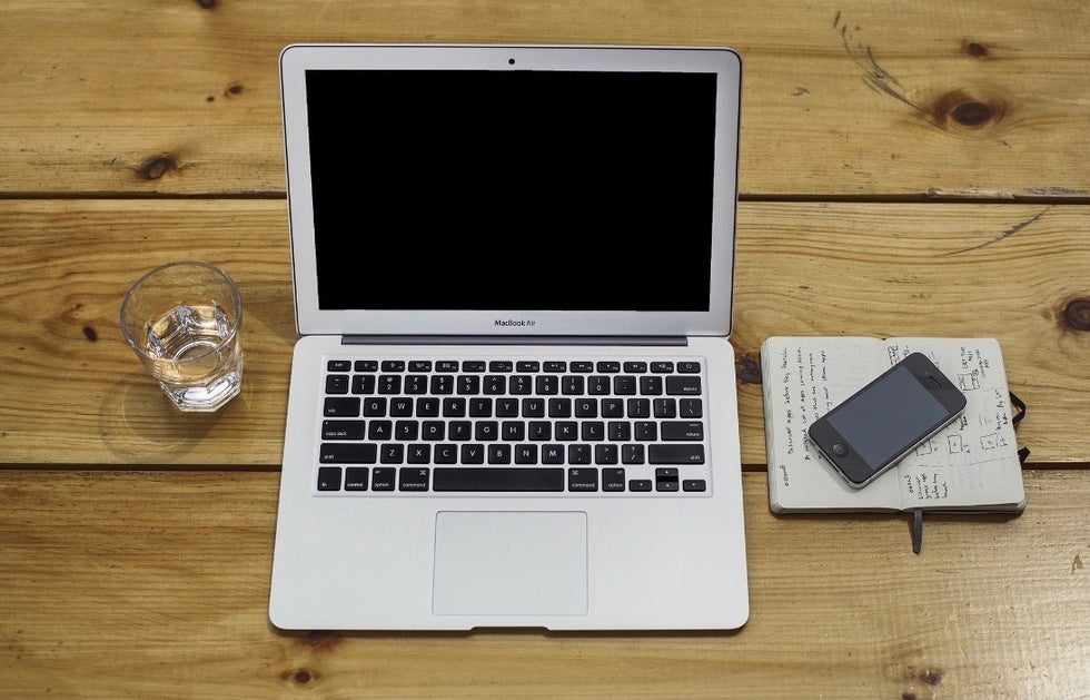 Wooden table with laptop, phone, and notebook on top.