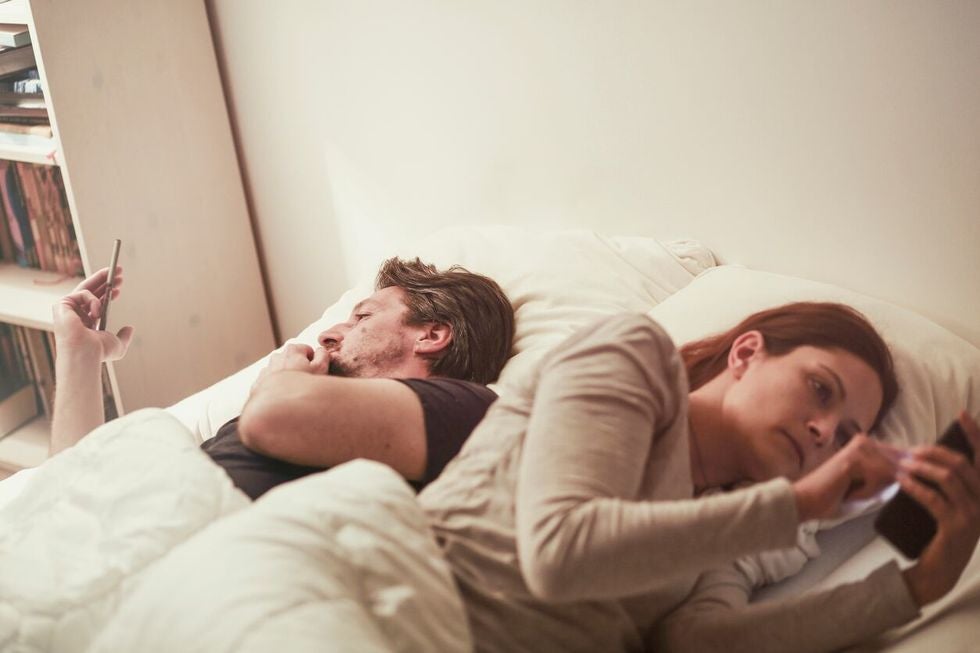 Man and woman laying in bed, both using their phones, turned away from each other,