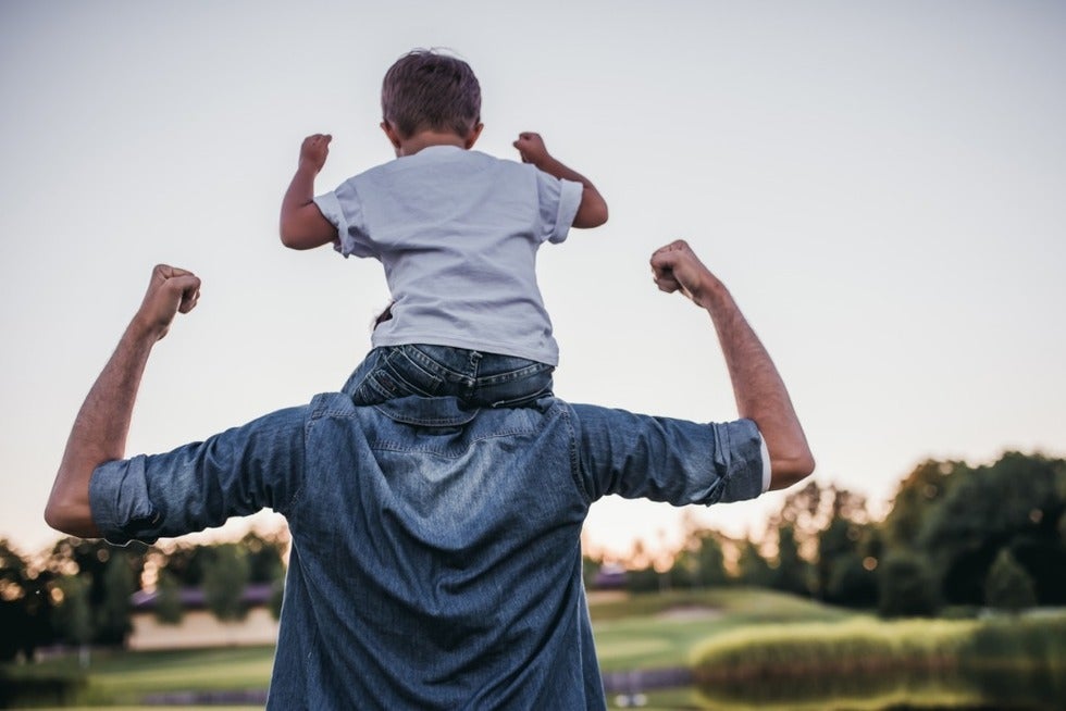 Man with his son sitting on his shoulders. Both flexing.